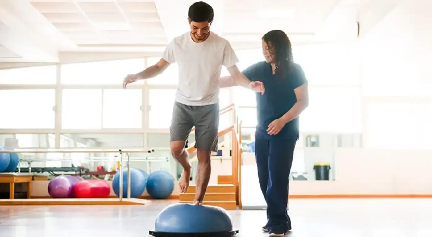 Physical therapist coaching a patient through single-leg balance training on a balance dome